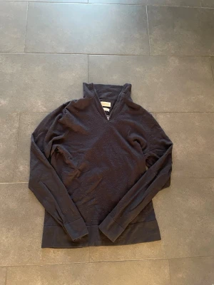 Mörkblå merinoullströja These Glory Days - Mörk, stilren mörkblå tröja från These Glory Days i mjuk merinoull. Tröjan har lång ärm, hög krage och en snygg half zip-dragkedja framtill. Perfekt för dig som gillar minimalistisk och clean stil.