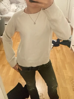 Vit stickad tröja med rund hals - Säljer en enkel och stilren vit stickad tröja med rundad hals och ribbade muddar vid ärmslut och nederkant. Tröjan har lång ärm och en normal passform, perfekt att matcha med jeans eller kjol. Supermjuk och skön för kyliga dagar.