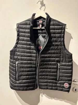 Dunväst, Colmar - Säljer en svart dunväst från Colmar Originals i italiensk storlek 46 (motsvarar europeisk 42 men fungerar även som en oversized väst på mig som är 36-38). Västen har quiltad design, två fickor med dragkedja och medelhög krage. Materialet är lätt och smidigt. Större logga framtill på ena sidan samt en mindre logga på baksidan på ena sidan. Nypris: 2 690kr