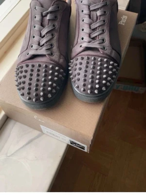 Grå Christian Louboutin sneakers med nitar - Säljer ett par riktigt schyssta Christian Louboutin skor. Skorna är i ett bra skick (bilderna e gamla kom prov om ni vill se dom nu) saknar dock en spik och vissa spikar har tappat lite färg men är lätt att lösa. Annars skriv om det är något du vill veta om skorna. Pris kan diskuteras. Byte kan hända.😁