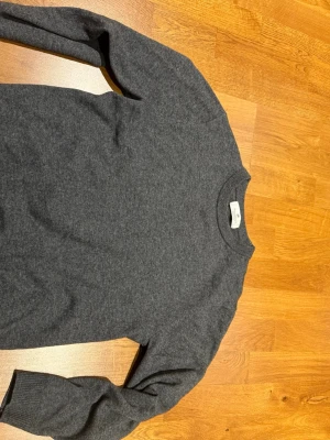 Mörkgrå stickad tröja i kashmir av H&M - Mysig mörkgrå stickad tröja från H&M med rund halsringning och långa ärmar. Klassisk och stilren modell som funkar året runt