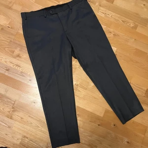 Mörkgrå kostymbyxor Dressman - Snygga mörkgrå kostymbyxor med klassisk rak passform. Modell: Trouser Bi-Stretch Grey. Använda 1 gång, nypris 799kr. Storlek: W40 L30. Midja: 109-114cm och Insida ben (plaggets mått): 74,2