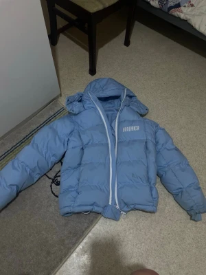 Blå pufferjacka från Hoodrich XS - Säljer en blå pufferjacka från Hoodrich i storlek XS. Jackan har huva, vit dragkedja och ett stilrent Hoodrich-tryck på bröstet. Perfekt för kalla dagar och har en riktigt skön, vadderad känsla. Fräsch och trendig färg som sticker ut.