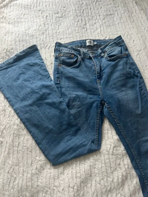 Blå flare jeans från 157 - Säljer ett par blå jeans från 157 med flare-ben och klassisk femficksdesign. Jeansen har hög midja och är tillverkade i mjukt denimtyg med ljusblå tvätt. Snygga kontrastsömmar och knappstängning framtill. Perfekta för dig som gillar retrovibbar och breda ben. Kortare längd på byxorna 