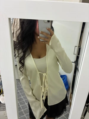 Krämvit omlottopp med snörning - Säljer en krämvit omlottopp i satinliknande material med långa ärmar och snygg snörning framtill. 