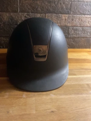 Svart Samshield hjälm 57M - Säljer en stilren svart hjälm från Samshield i storlek 57M. Hjälmen har en matt finish, diskret logga framtill i metall och bekväm vaddering på insidan. Jättefin använd men i bra skick, inga skador!!❣️❣️priset går absolut att diskutera❣️