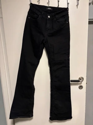 Svarta bootcut jeans från ONLY - Säljer ett par svarta jeans från ONLY med klassisk femficksmodell och bootcut-ben. Jeansen har normal passform och är tillverkade i ett mjukt bomullsmaterial med lite stretch. Perfekta till sneakers eller boots för en avslappnad look.