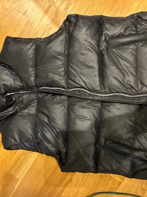 Svart dunväst från Filippa K - Säljer en svart dunväst från Filippa K i storlek S. Västen har en quiltad design med dragkedja framtill och praktiska fickor. Perfekt för lager-på-lager och ger en clean och stilren look. Materialet är syntet och dun, vilket gör den både lätt och varm.