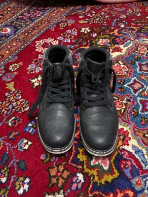 Svarta boots med snörning och grå detalj - Svarta boots med snörning och robust sula. Ovandelen är i skinnliknande material med grå mockadetalj runt ankeln. Skorna är använda ett fåtal gånger men passade inte