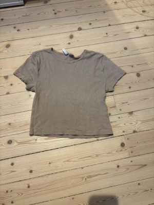 Beige ribbad croppad t-shirt - Säljer en beige croppad t-shirt med ribbad struktur och rund hals. T-shirten har korta ärmar och är enkel men ändå snygg, perfekt för att matcha med jeans eller kjol. Materialet känns mjukt och skönt mot huden.