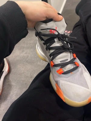 Nike Jordan sneakers grå och orange - Säljer ett par Nike Jordan sneakers i grått med orange detaljer och svart snörning. Skorna har en rund tå, platt sula och meshpaneler på sidorna. Insidan är svart med röd Jumpman-logga. Snygg design med kontrasterande färger och slitstark syntetmaterial.