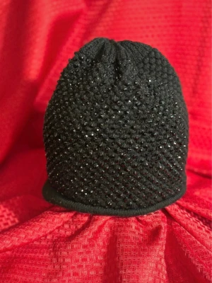 Svart stickad mössa med paljetter , huvudvolym 42cm , akryl 80%, polyester 20% - Svart stickad mössa med glittriga paljetter över hela ytan. Mössan har en rundad form och är tillverkad i ett mjukt stickat material som känns skönt mot huvudet. Perfekt för dig som gillar att sticka ut med lite extra bling.