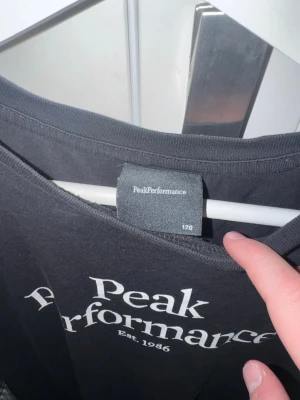 Svart Peak Performance t-shirt - Säljer en svart t-shirt från Peak Performance med vit logga och text 'Est. 1986' på bröstet. Klassisk rund hals och korta ärmar. Perfekt basic-plagg med snygg passform och stilren design.