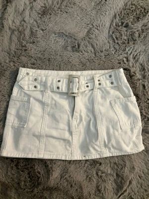 Vit miniskirt  -  Säljer en vit miniskirt med brett bälte och fickor! Kjolen är i jeans. Kjolen är väldigt kort och är i XXS-XS.