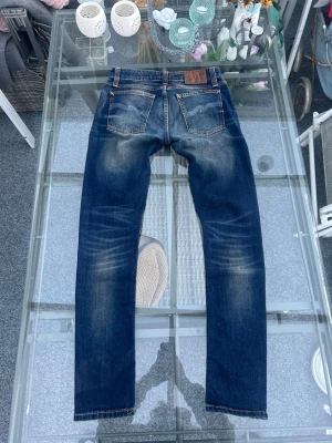 Nudie Jeans Skinny Lin – Dark Double Indigo (W29/L32) - Snygga Nudie Jeans Skinny Lin i mörkblå dark double indigo. Tight/skinny passform med stretch som sitter riktigt bra och är bekväm hela dagen. Klassisk mörk denim med schyssta fades vid knän och lår – clean look som funkar till allt från hoodie till skjorta.  Tillverkade i ekologisk bomull med elastan för bättre komfort och hållbar kvalitet. Perfekta om du gillar slim fit, streetwear, minimal stil eller vill ha ett par jeans som funkar både till vardag och kväll.  Storlek: W29 L32 Modell: Skinny