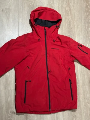Peak Performance skidjacka strl M - Maroon Hipe® 2L Insulated Shell Jacket Herr – Peak Performance  Vind- och vattentät skidjacka i tvålagers Hipe®-material med hög andningsförmåga och tvåvägsstretch. Syntetisk vaddering för värme, ventilationsdragkedjor under ärmarna och förböjda ärmar för bra rörlighet. Justerbar huva (hjälmkompatibel), snölås med snap-in samt flera praktiska fickor, bl.a. liftkortsficka. I mycket fint skick, endast en liten minireva på vänster axel (se bild 6) Nypris: 3500 kr