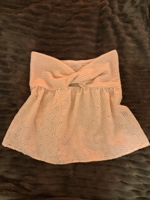 Vit bandeau tubtopp från SHEIN - Säljer en vit bandeau tubtopp från SHEIN i storlek S. Toppen har en virkad, ribbad överdel med twistdetalj framtill och en broderad, blommig nederdel i bomull. Perfekt för sommarens alla tillfällen, superfin till jeans eller kjol.