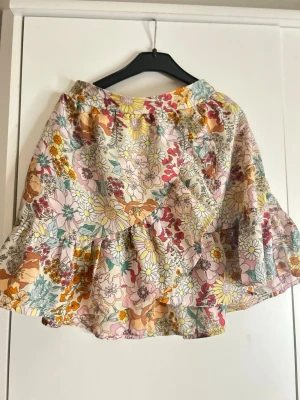 Blommig volangkjol från H&M - Säljer en superfin kort kjol från H&M i storlek 146/152 med blommigt mönster i pastellfärger som rosa, gul, grön och orange. Kjolen har volanger och resår i midjan för skön passform. Perfekt för dig som gillar färgglada plagg!
