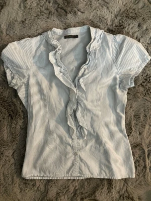 En blå vit randig blus!  - En jättegullig  blå vit randig blus/skjorta! Med fin volang! I storlek 34. Passar jättebra till sommaren! 