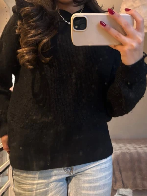 Svart hoodiestickad tröja i alpacka - Mysig svart stickad tröja med rund hals och långa ärmar. Enkel och stilren design som passar perfekt till jeans eller andra favoritplagg. Tröjan har en normal passform och är tillverkad i ett mjukt stickat material (alpacka) som håller dig varm under kyliga dagar. Tröjans luva är väldigt gosig.