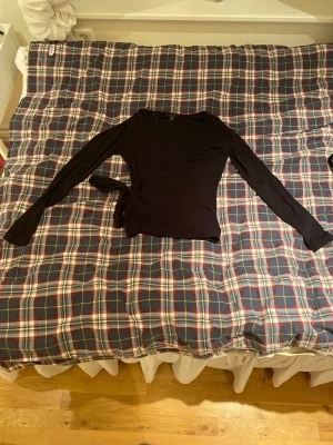 Svart omlottopp från Amisu - Säljer en svart omlottopp från Amisu i storlek S. Toppen har långa ärmar, v-ringning och knyt i sidan för en snygg passform. Perfekt till jeans eller kjol och enkel att styla med accessoarer. Har aldrig använt tröjan och ångrade mitt köp det är därför jag säljer den 💕