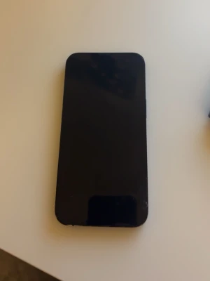 iPhone 13 - Säljer en svart iPhone 13. Återställer den innan jag skickar iväg den.Telefonen har dubbla bakre kameror och fungerar utmärkt. Skärmen och baksidan visar mindre slitage, särskilt i kanterna. Perfekt för dig som vill ha en pålitlig och kraftfull smartphone.