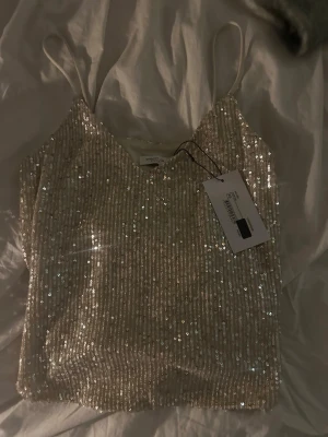 Glittrig paljettlinnetopp från Stockh LM Studio - Säljer en snygg glittrig linnetopp från Stockh LM Studio i ljus champagnefärg. Toppen har tunna axelband och är täckt med paljetter som ger ett riktigt festligt intryck. Perfekt att styla med jeans eller kjol för en trendig look.