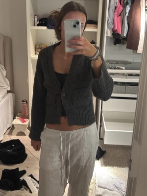 Mörkgrå stickad kofta med knappar - Säljer en mysig mörkgrå stickad kofta med stora knappar framtill och två fickor. Koftan är croppad och har långa ärmar med breda muddar. Perfekt att slänga på sig över ett linne eller t-shirt för en chill look. Säljer då den är alldeles för liten💕