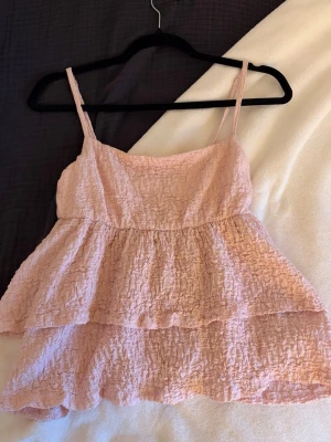 Ljusrosa volangtop från Gina Tricot - Säljer en ljusrosa topp från Gina Tricot i storlek S. Toppen har smala axelband, dubbla volanger och ett krinklat tyg.