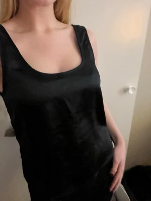 Svart linnetopp i satin-look - Säljer en svart linnetopp med breda axelband och rundad urringning. Toppen har en snygg satin-liknande finish som ger en stilren och trendig vibe. Perfekt att styla med jeans eller kjol för en clean look. Orginalpris: 299kr