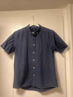 Blå kortärmad skjorta från Ellos - Säljer en stilren blå skjorta från Ellos i storlek S. Skjortan har korta ärmar, klassisk krage med knappar och en bröstficka. 