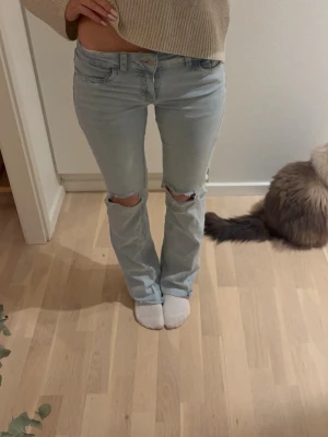 Ljusblå bootcut jeans med hål - Säljer ett par lågmidjade ljusblå jeans med bootcut passform och slitna hål över knäna. Perfekt längd för mig som är 160 men passar folk som är något längre❤️ skriv vid frågor pris kan diskuteras 