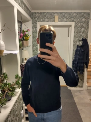 Mörkblå stickad tröja i bomull - Säljer en mörkblå stickad tröja med rund hals och ribbade muddar. Tröjan är tillverkad av 100% ekologisk bomull och har en klassisk, enkel design som funkar till jeans eller andra byxor. Perfekt för dig som gillar stilrena och bekväma plagg.