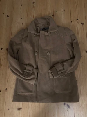 Beige kappa från Isolde🫶🏻 - Snygg beige kappa från Isolde i ullmix med dubbelknäppning och stora dekorativa knappar. Jackan har bred krage, markerade fickor och fina detaljer vid ärmsluten samt bälte i ryggen. Perfekt för höst och vinter när du vill vara både varm och stilren. En knapp har trillat av, men den finns kvar har dock inte sytt på den eftersom jag ont heat haft orken. Om det krisar kan jag göra det innan jag skickar den🤍