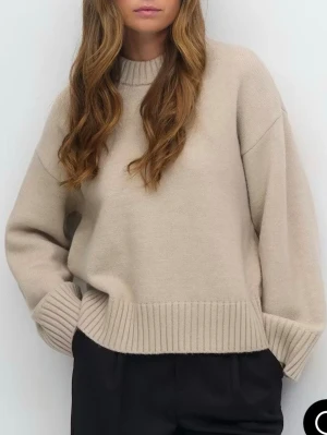 Beige stickad tröja från Glamroot - Säljer en beige stickad tröja från Gina som är helt ny med bred ribbad kant vid hals, ärmslut och nederkant. Tröjan har en loose passform och långärmade ärmar, perfekt för lager på lager. Enkel och stilren design som är lätt att matcha med olika outfits.