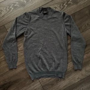 Grå stickad tröja från Oscar Jacobson - Mjuk och stilren grå stickad tröja från Oscar Jacobson. Klassisk rund halsringning och ribbade muddar vid ärmslut och nederkant. Perfekt till lager på lager under höst och vinter. Enkel att matcha med både jeans och chinos.