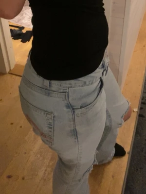 Bootcut jeans med låg midja från Nelly - Bootcut jeans i ljusblå denim med låg midja. Nelly jeans med rosa brodroderingar baktill. Liten fläck där bak. 