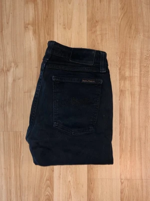 Nudie Jeans - Säljer ett par svarta jeans från Nudie Jeans. Jeansen har smal passform och är tillverkade i mjukt bomullsmaterial med stretch. Midja 34cm, längd 99cm. JAG SKICKAR EJ FLER BILDER NÄR JAG BÄR JEANSEN! för bättre inblick i passformen rekommenderar jag att googla på modellnamnet. För storleksguide kolla måtten noggrant då jeansen alltid kan vara uppsydda heller krympta och jag ej tar emot returer :) s5,4
