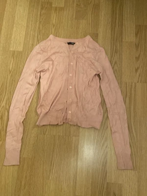 Ljusrosa kofta från 157 XS - Säljer en ljusrosa kofta från 157 i storlek XS. Koftan har rund hals, långa ärmar och knappar framtill. Materialet är mjukt och känns som bomull, perfekt för lager-på-lager. Ribbstickade muddar vid ärmslut och nederkant ger en snygg passform.