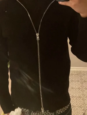 Svart kofta med dragkedja från Ljung - Snygg svart kofta från Ljung by Marcus Larsson i storlek M. Koftan har en hel dragkedja framtill och är långärmad med en stilren look. Perfekt att slänga på sig när det är lite kyligare ute. Passar dig som gillar minimalistisk design och svart basic.