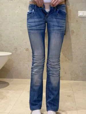 Blå bootcut jeans med rynkade knän - Säljer ett par blå jeans med bootcut passform och snygga rynkade detaljer vid knäna. Jeansen har låg midja, är i storlek 24. Köpt på Plick, lånade bilder!!☺️