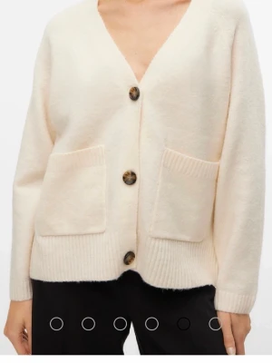 Beige stickad kofta med knappar - Mysig vit/beige stickad kofta från Vero Moda med framfickor och snygga bruna knappar. Koftan har v-ringad hals och ribbade muddar vid ärmslut och nederkant. Perfekt för lager-på-lager under kyliga dagar. Den är använda men inga defekter. Säljer en likadan i svart. Storlek Xs men passar mig perfekt som vanligtvis är en M/S. ORIGINAL PRIS: 449kr!!! NYPRIS: 200kr
