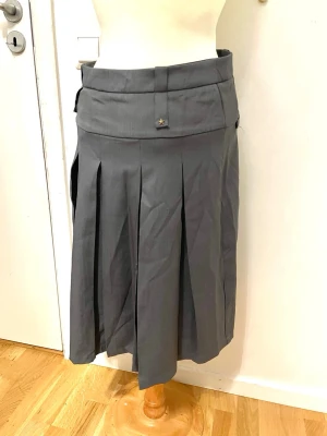 Grå plisserad långkjol med stjärndetalj - Snygg grå långkjol med bred linning och plisserade veck som ger en cool och stilren look. Kjolen har små stjärndetaljer på linningen och är gjord i ett mjukt och lätt bomullsmaterial. Perfekt för dig som gillar minimalistisk stil och vill ha något som sticker ut lite.