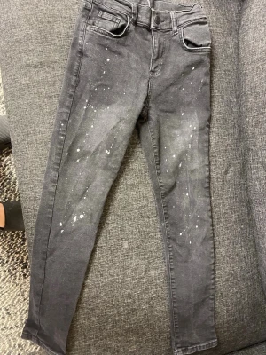 Mörkgrå skinny jeans med stänk - Säljer ett par mörkgrå skinny jeans med coola vita färgstänk på framsidan. Jeansen har klassisk femficksdesign, normal midja och smal passform hela vägen ner. Materialet är mjukt och stretchigt för extra komfort.