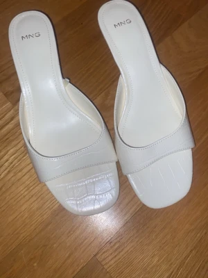 Vita sandaler med låg klack från MNG - Säljer ett par stilrena vita sandaler från Mango med låg klack och fyrkantig tå. Perfekta för dig som gillar minimalistisk och trendig design. Använda 1 gång