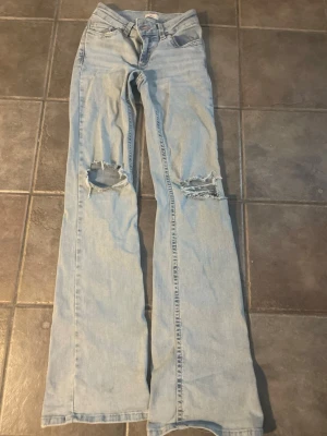 Bootcut jeans från Nelly med slitningar - Bootcut jeans i ljusblå färg från nelly. Ny pris är ca 600 kr. De har hål på knäna och rosa mönster på fickorna. Tyvärr är jeansen söndriga med hål längst ner på jenasen, inget man tänker på. Därför går priset att diskuteras men start priset är 300. Storlek 32.