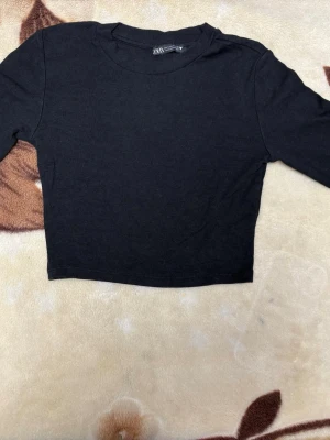 Svart långärmad magtröja från Zara - storlek S  - En jättefin svart långärmad crop top från Zara i storlek S. Den är ganska liten i storleken och passar även en XS. Materialet är ribbat, väldigt stretchigt och figurnära vilket ger en superbra passform. Rund halsringning och slim fit. Materialetiketten är avklippt så är osäker på exakt innehåll, men det känns som en mjuk bomullsmix. Mycket bra skick! Perfekt basplagg till allt. Kolla gärna in min profil, jag erbjuder bundlepris vid köp av flera varor! 