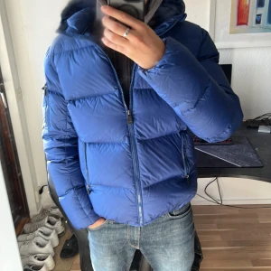 Blå dunjacka från JOTT - Snygg blå dunjacka från Jott (Just Over The Top) med huva och dragkedjor på fickorna. Jackan är quiltad och har en klassisk puffer-look med logga på ärmen. Perfekt för kalla dagar och riktigt skön att bära. Jag har aldrig frusit när jag haft på mig denna jacka. Priset går att förhandla!