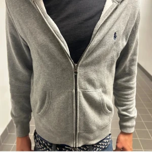 Grå hoodie från Polo Ralph Lauren - ❗️Pris kan diskuteras❗️ Säljer en stilren grå hoodie från Polo Ralph Lauren med dragkedja och klassisk broderad logga på bröstet. Tröjan har huva, kängurufickor och är tillverkad i mjuk bomullsmix. Perfekt för chill dagar och enkel att matcha med jeans.