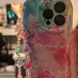 iPhone 14 Pro - Snygg iPhone 14 Pro med färgglatt skal och matchande pärlband. Skalet har texten 'Happy every day' och är i mycket gott skick utan repor. Denna skal fick jag i present men det var tyvärr inte min stil. Perfekt för dig som vill ha en unik och personlig look. Köptes för 250kr men säljs för 70kr